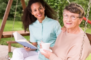elder woman holding a cup of coffee with her caregiver holding a book